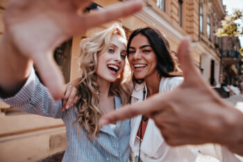 Two women smiling through a heart shape made with their hands