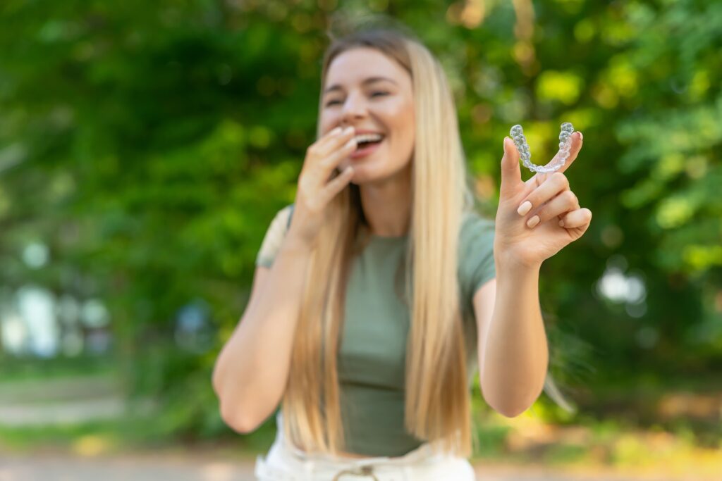 Woman holding a clear dental aligner outdoors