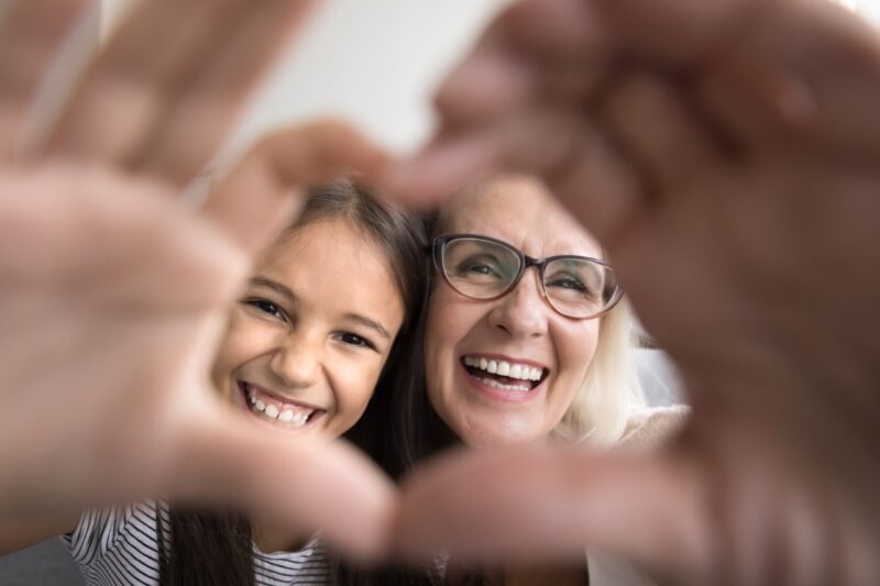 Two women smiling through a heart shape made with their hands